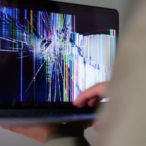 A close-up view of a cracked laptop screen displaying colorful digital distortion.