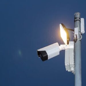 Low angle view of a security camera and light against a dark blue night sky.