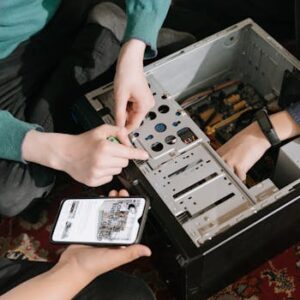 A close-up of hands fixing a computer with guidance from a mobile device.